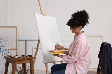 Photo of Young woman mixing paints on palette near easel in studio