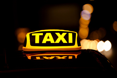 Taxi car with yellow roof sign on city street at night, closeup