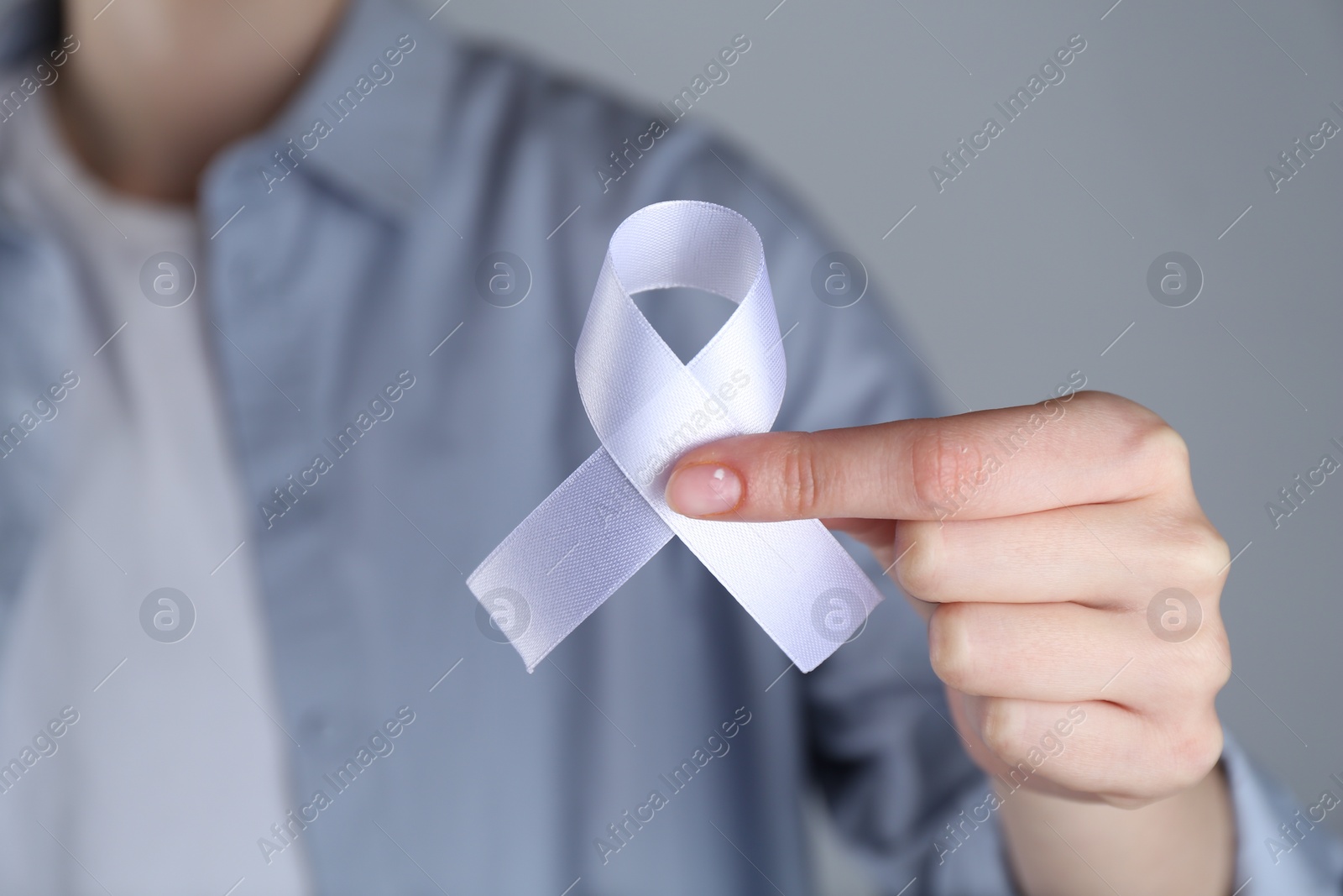 Photo of Woman holding white awareness ribbon on grey background, closeup