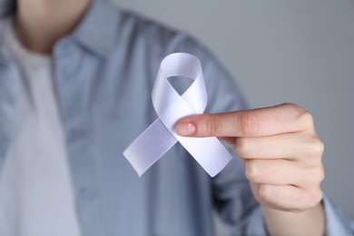 Woman holding white awareness ribbon on grey background, closeup