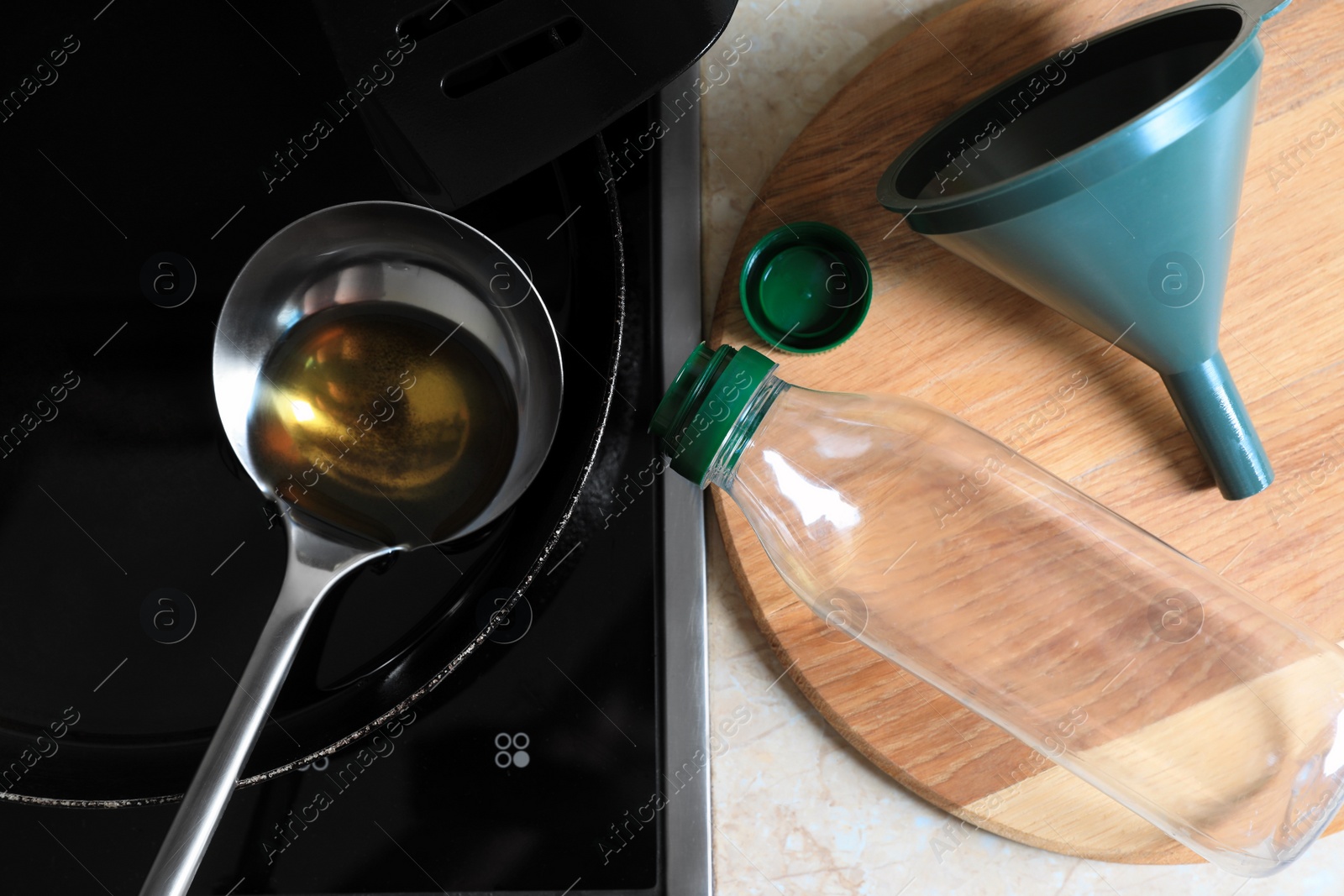 Photo of Frying pan of used cooking oil with ladle, empty bottle and funnel in kitchen, flat lay