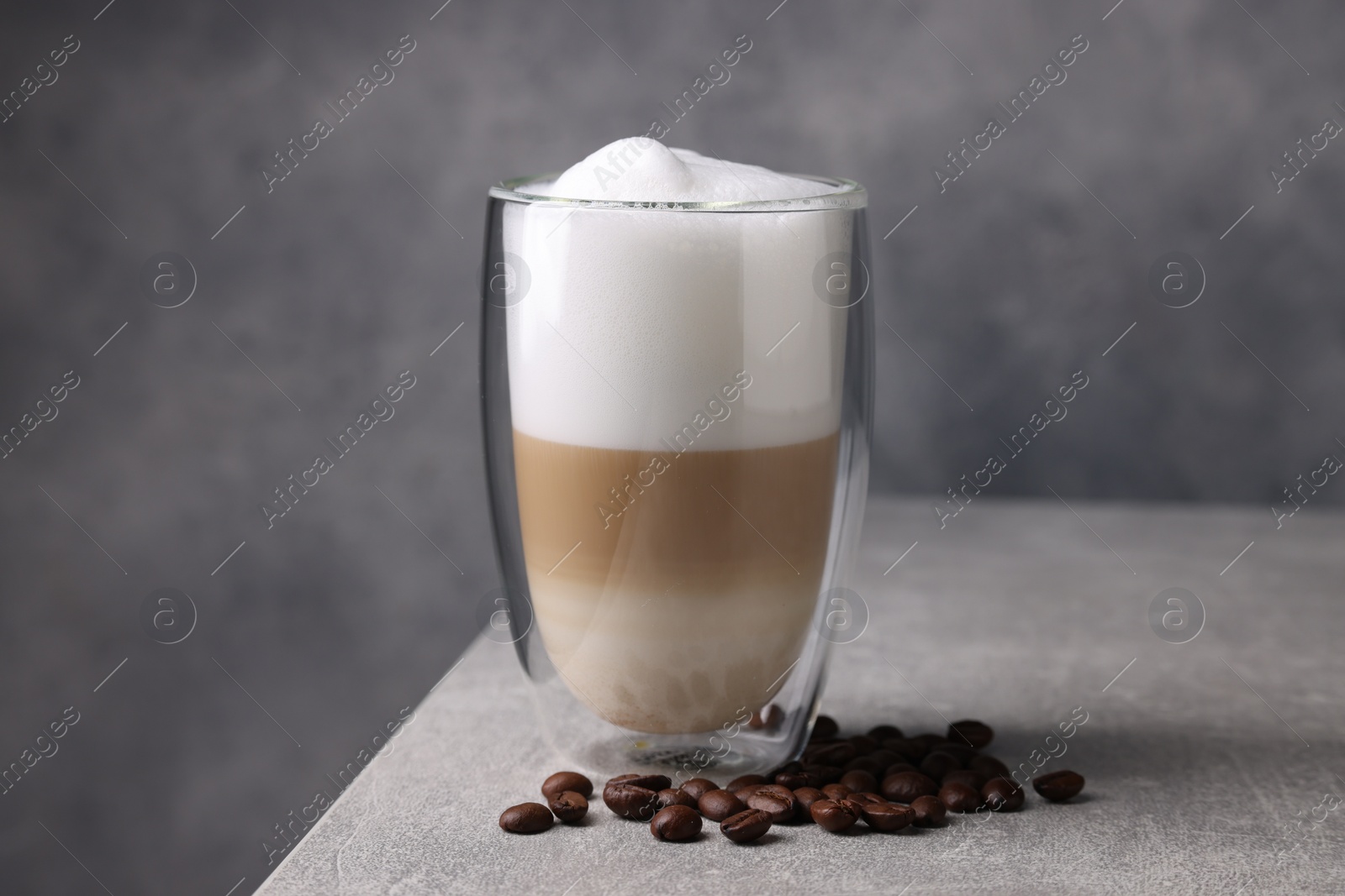 Photo of Aromatic latte macchiato in glass and coffee beans on light grey table