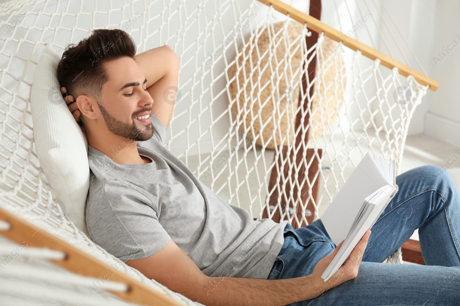 Photo of Young man reading book in hammock at home