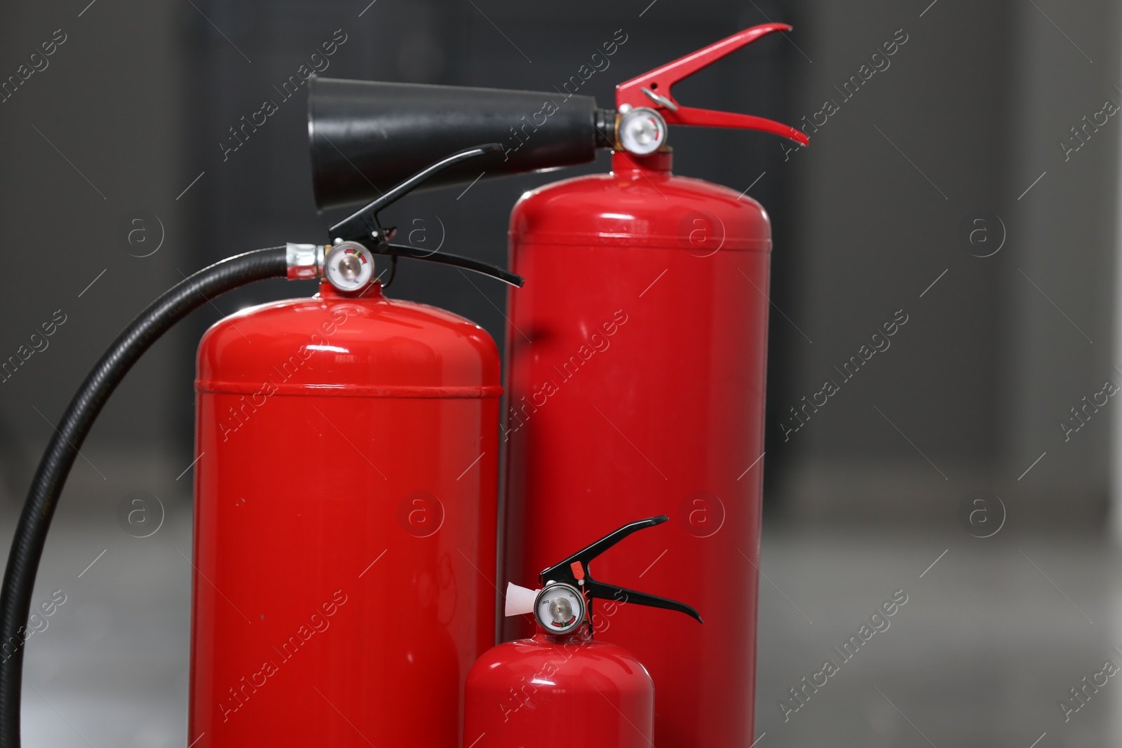 Photo of Three new red fire extinguishers in hall, closeup. Space for text