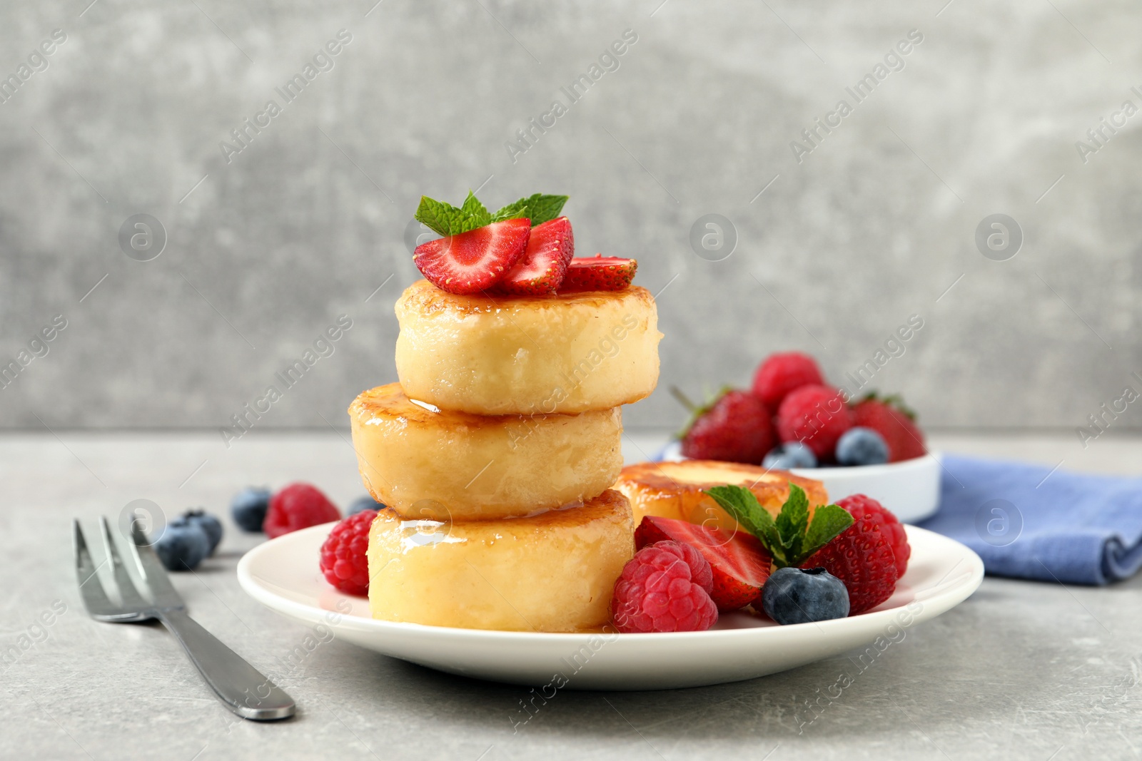 Photo of Delicious cottage cheese pancakes with fresh berries, mint and honey on light grey table