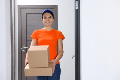 Photo of Smiling courier with cardboard boxes in hallway, space for text