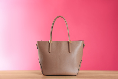 Stylish woman's bag on wooden table against pink background