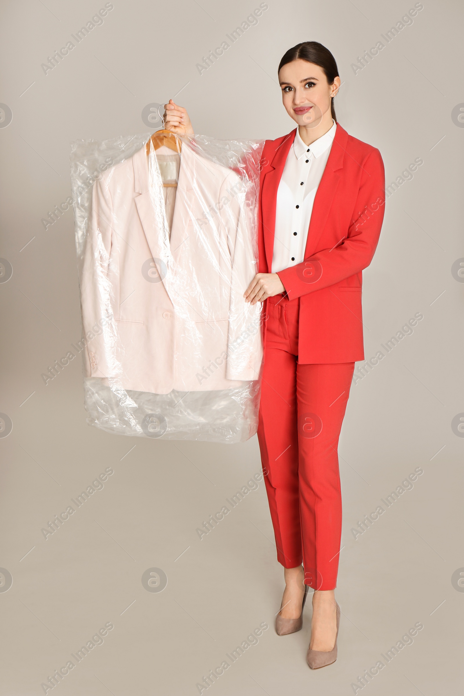 Photo of Young woman holding hanger with jacket on light grey background. Dry-cleaning service