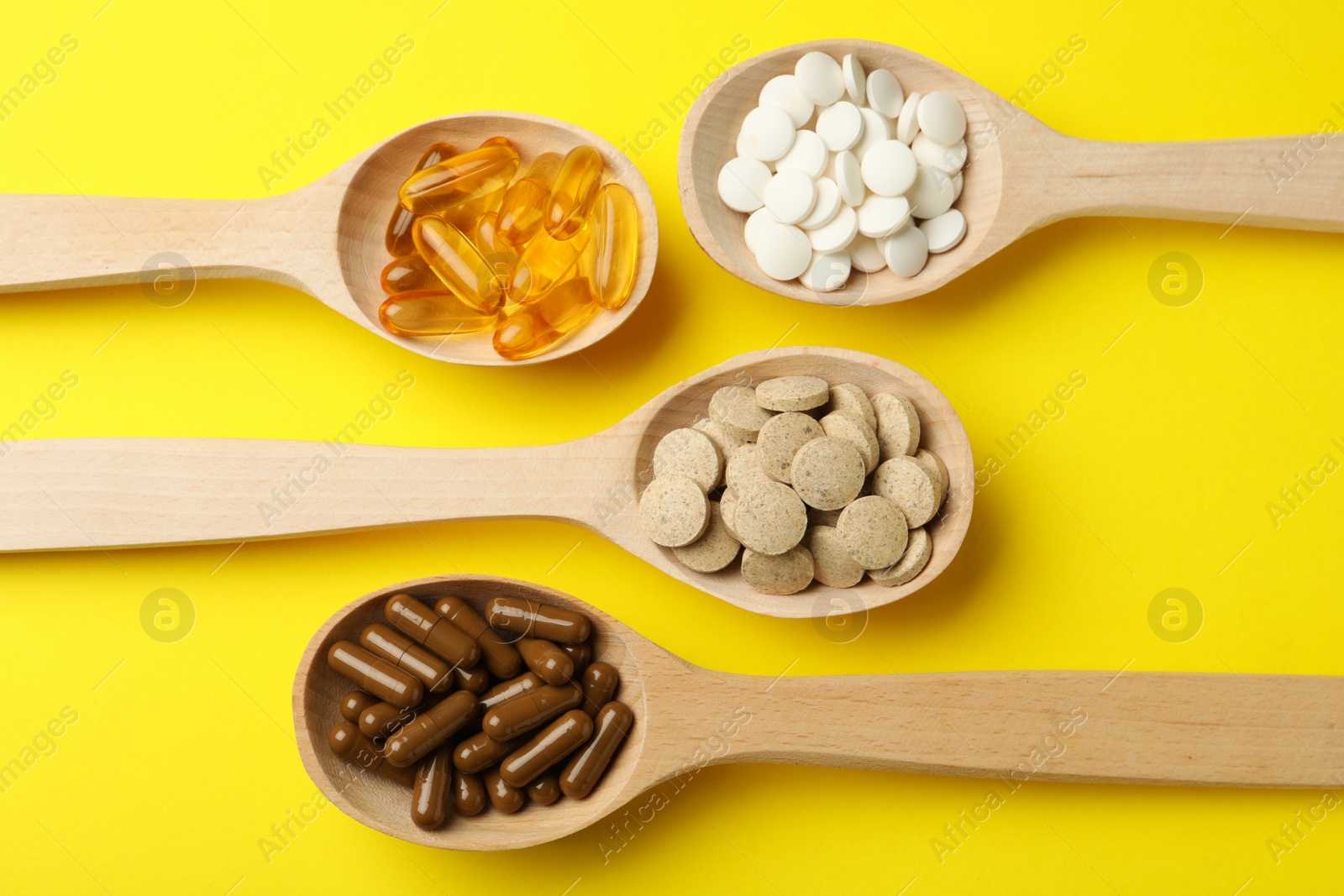 Photo of Wooden spoons with different dietary supplements on yellow background, flat lay