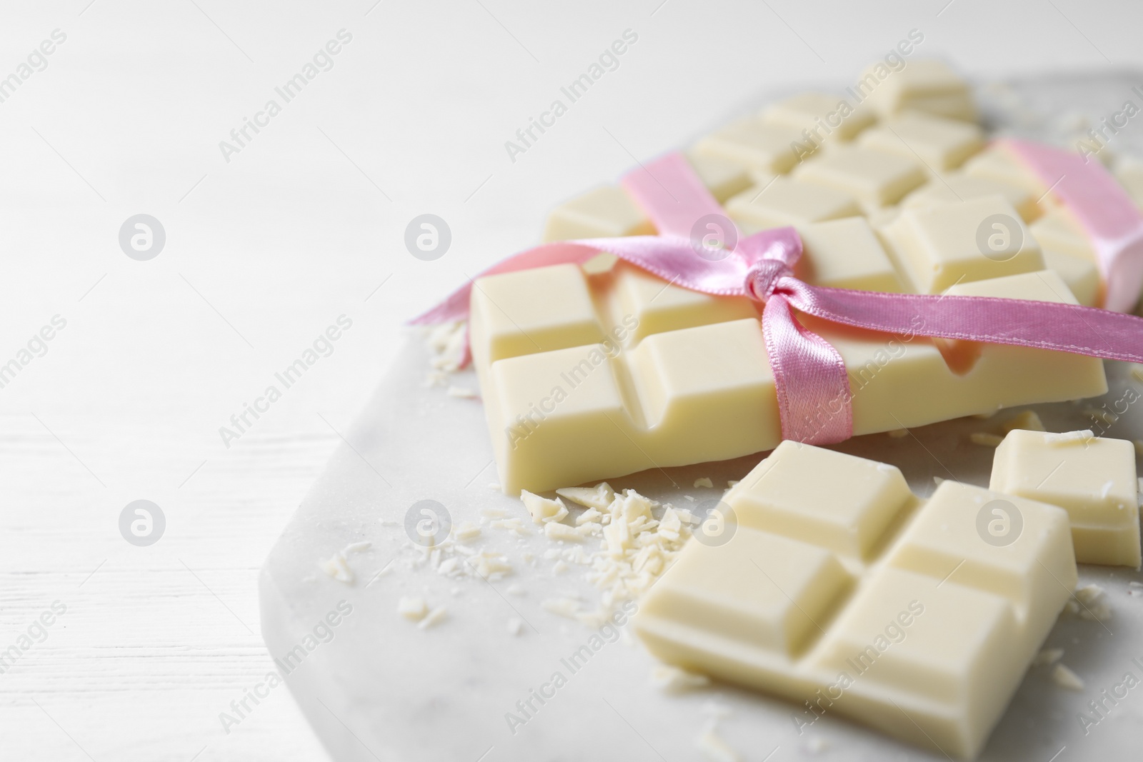 Photo of Tasty white chocolate with ribbon on wooden table, closeup