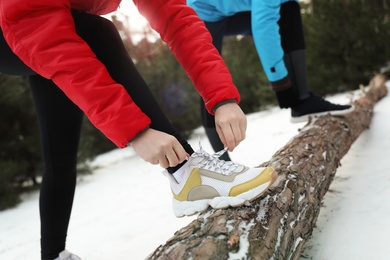 People lacing sneakers on log in winter forest, closeup. Outdoors sports exercises 