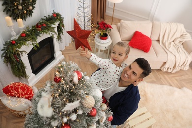 Father and little daughter decorating Christmas tree with star topper in room, above view