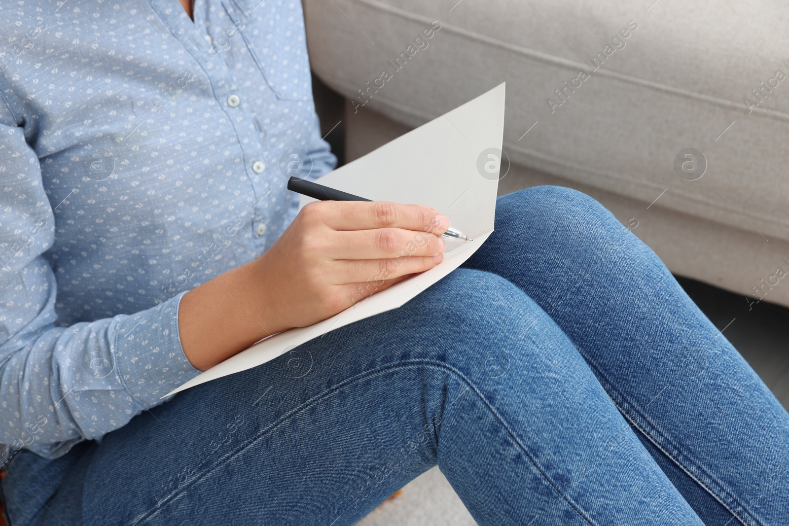 Photo of Young woman writing message in greeting card on floor, closeup