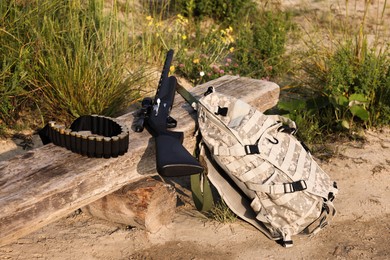 Hunting rifle, backpack and cartridges on wooden bench outdoors