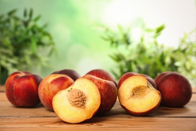 Photo of Fresh juicy peaches on wooden table against green blurred background, space for text