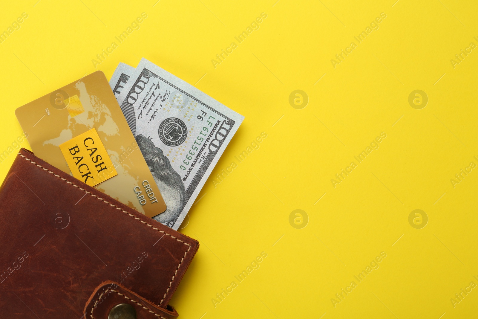 Photo of Dollar banknotes and credit card in wallet on yellow background, top view with space for text. Cashback concept