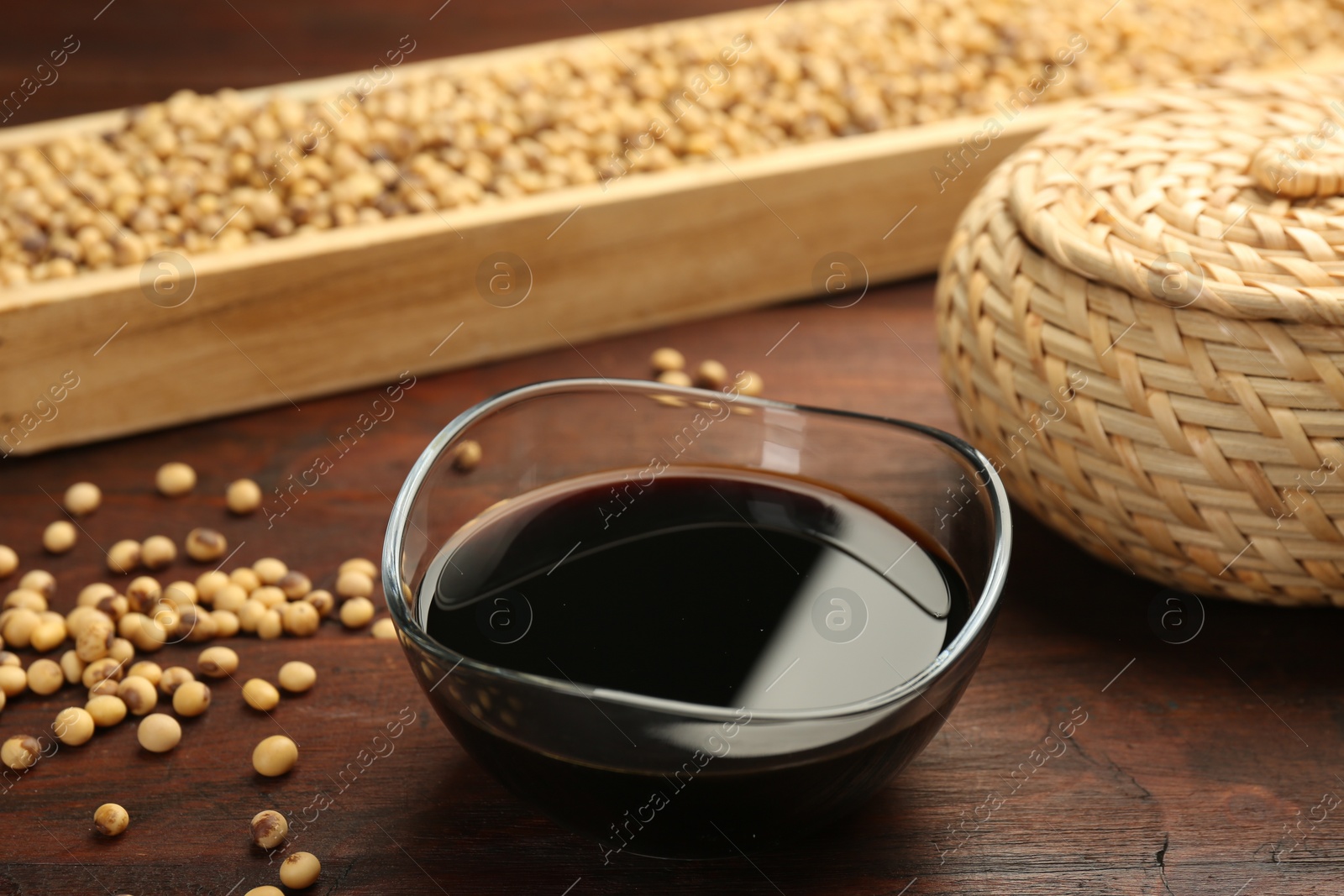 Photo of Soy sauce in bowl and soybeans on wooden table