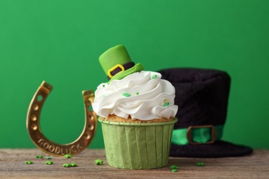 St. Patrick's day party. Tasty cupcake with leprechaun hat topper and gold horseshoe on wooden table