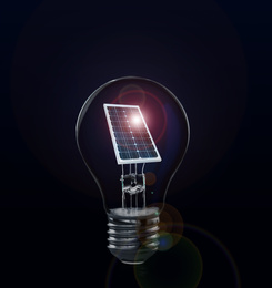 Image of Alternative energy source. Light bulb with solar panel on dark background 