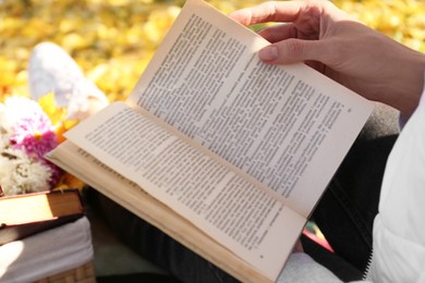 Photo of Woman reading book outdoors on autumn day, closeup
