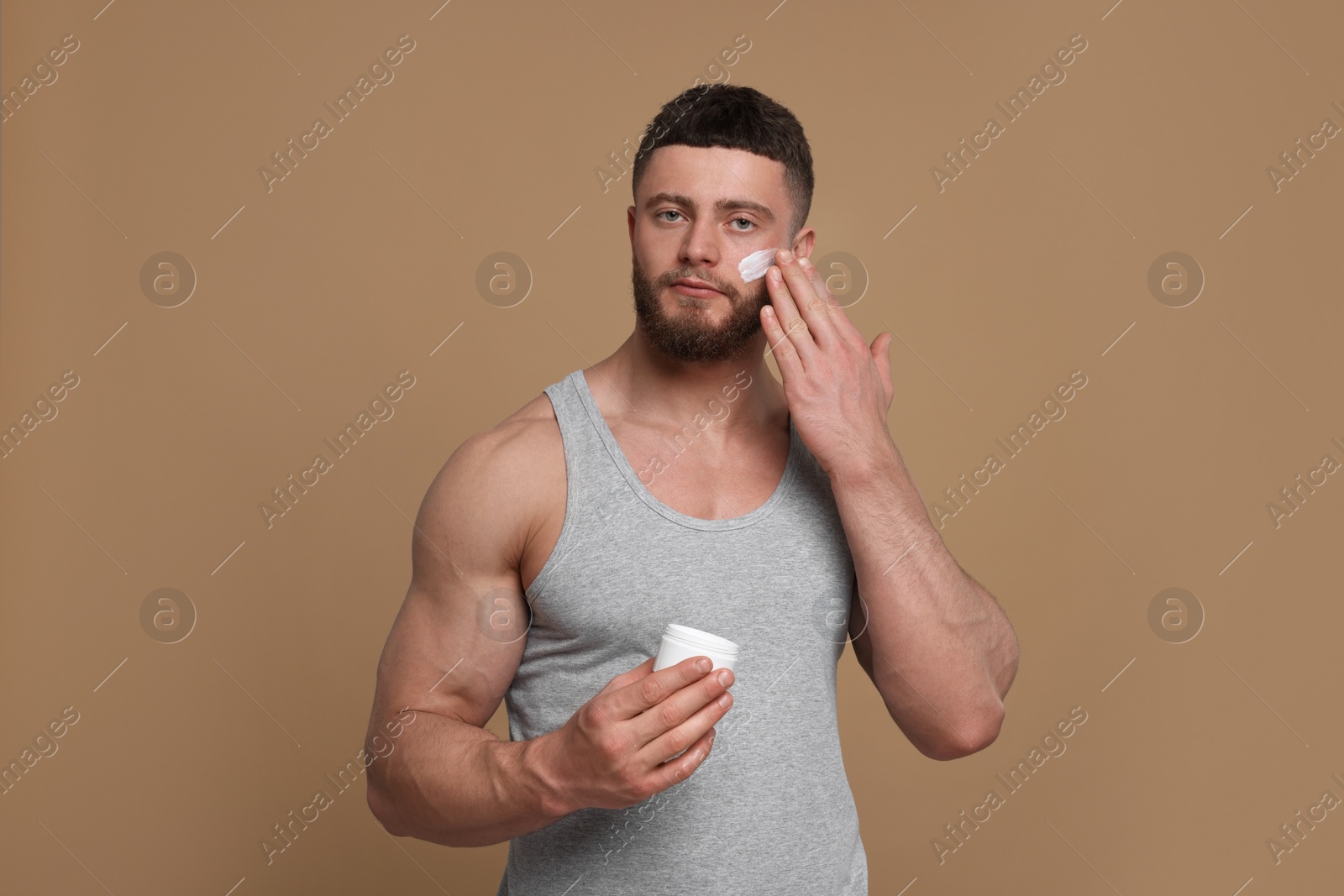 Photo of Handsome man applying cream onto his face on pale brown background