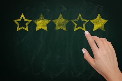 Quality evaluation. Woman touching golden star on green chalkboard, closeup