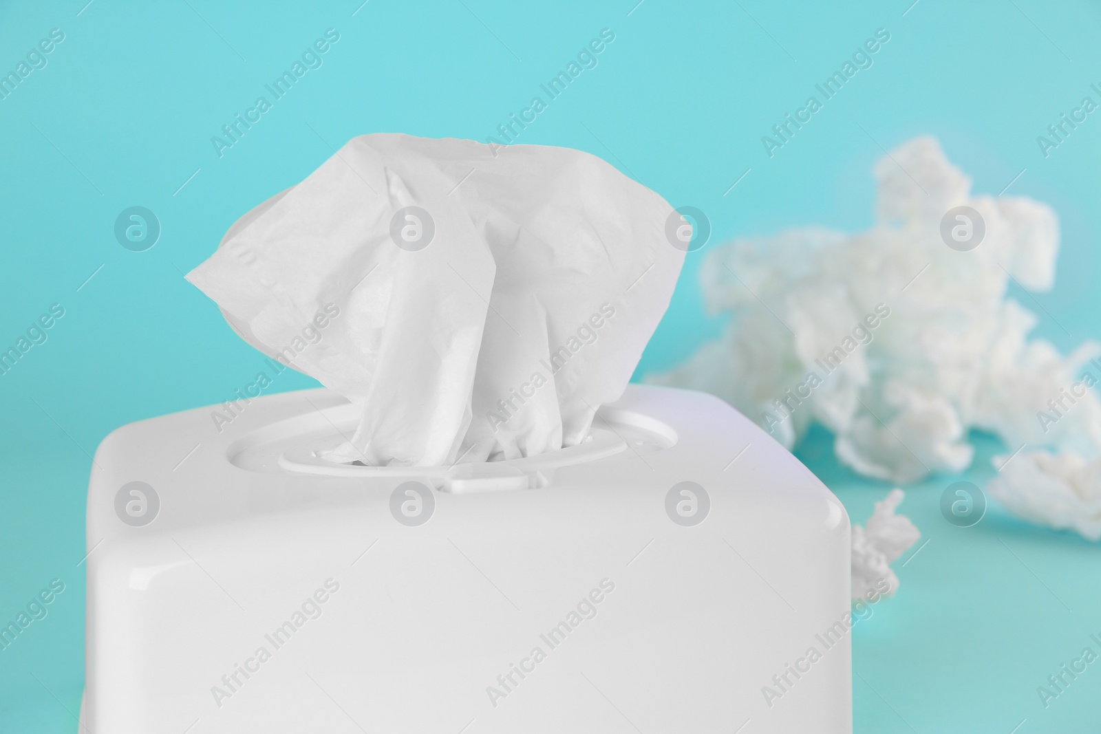 Photo of Used paper tissues and white holder on light blue background, closeup