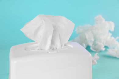 Photo of Used paper tissues and white holder on light blue background, closeup