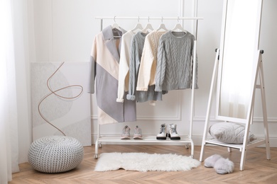 Rack with stylish warm clothes and mirror in dressing room