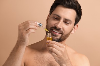 Smiling man with cosmetic serum on beige background, closeup