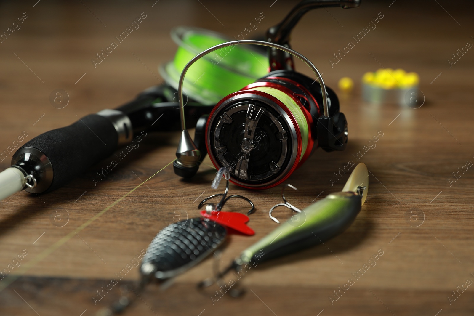 Photo of Fishing rod with spinning reel and baits on wooden background, closeup