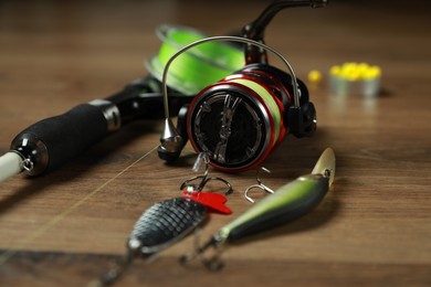 Fishing rod with spinning reel and baits on wooden background, closeup