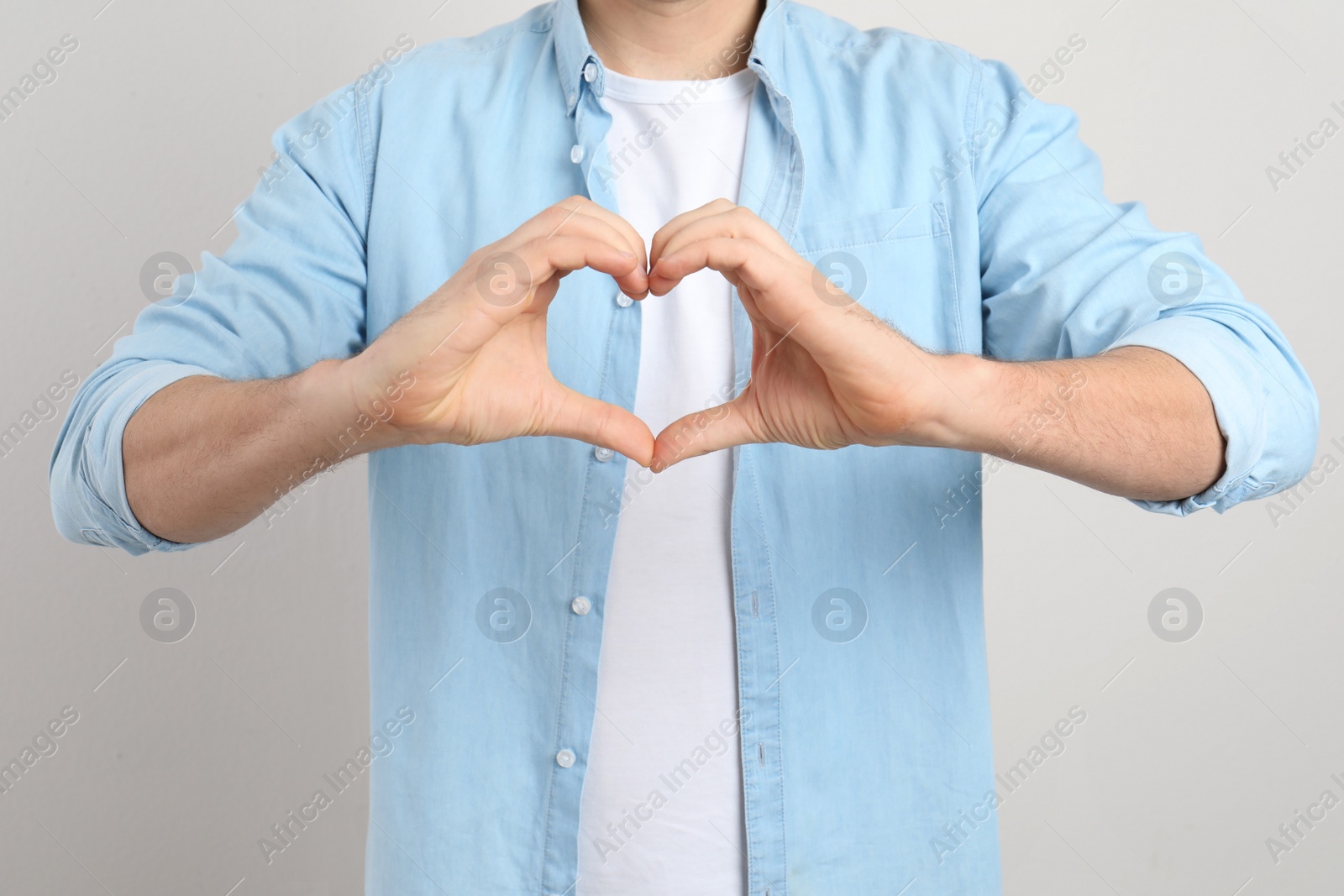 Photo of Man making heart with his hands on light background, closeup