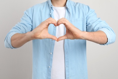 Photo of Man making heart with his hands on light background, closeup