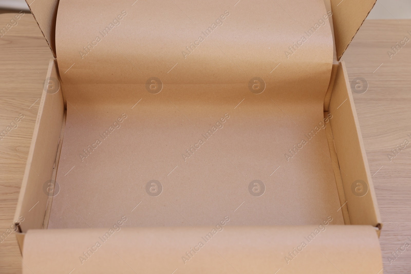 Photo of Empty cardboard box with kraft paper on wooden table. Delivery service