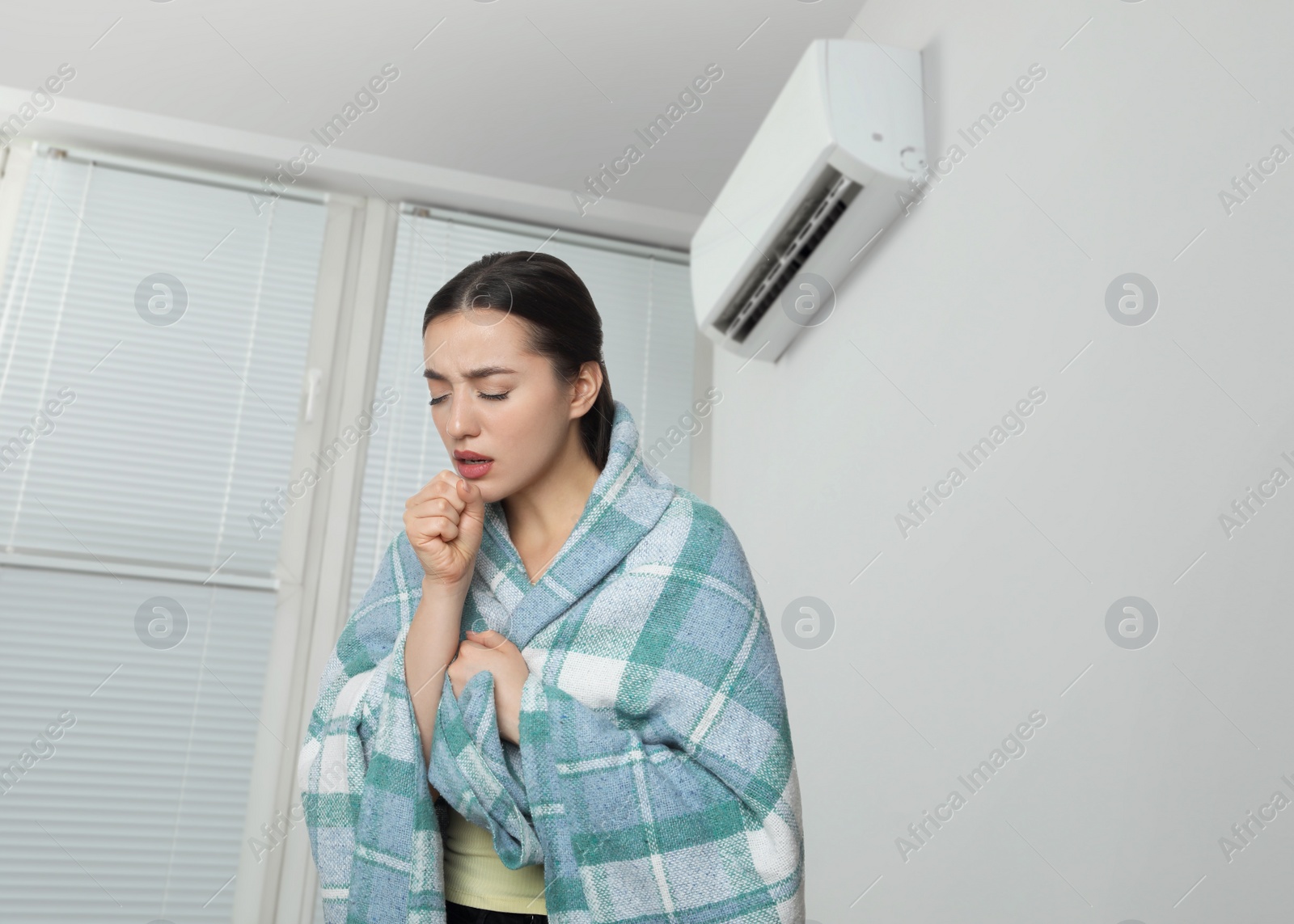 Image of Woman suffering from cold in room with air conditioner on white wall