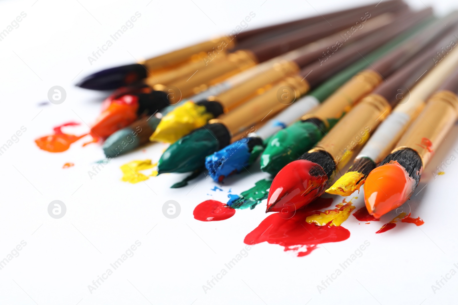 Photo of Brushes with colorful paints on white background, closeup