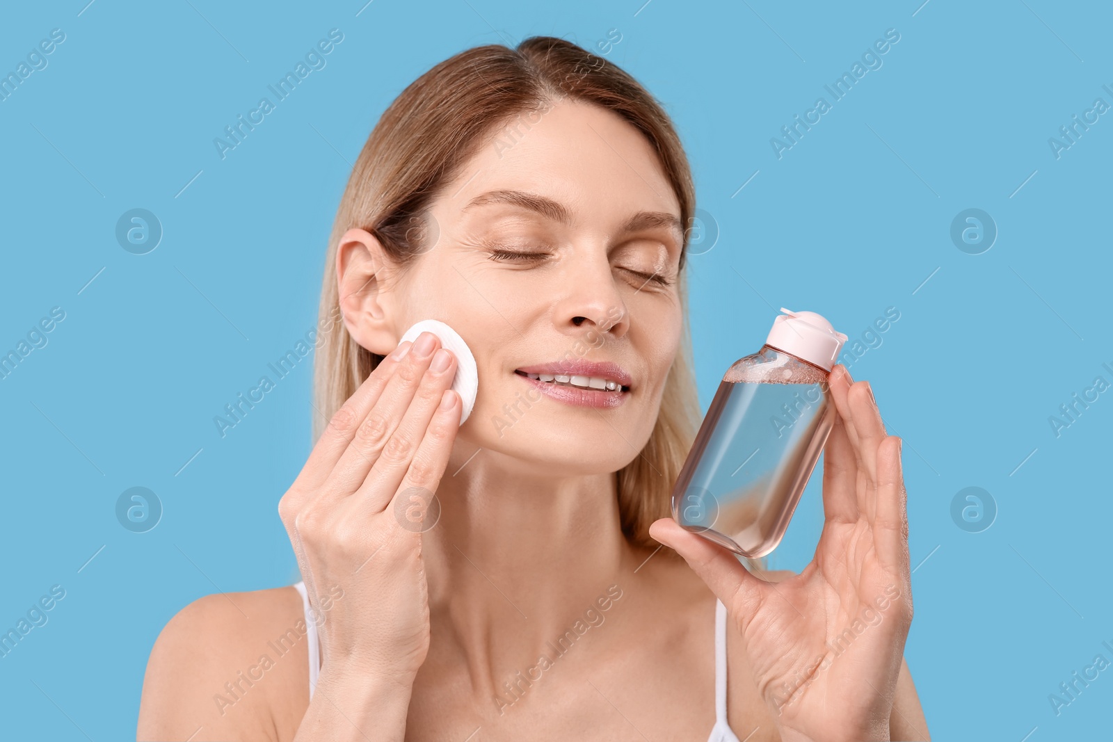 Photo of Beautiful woman removing makeup with cotton pad on light blue background