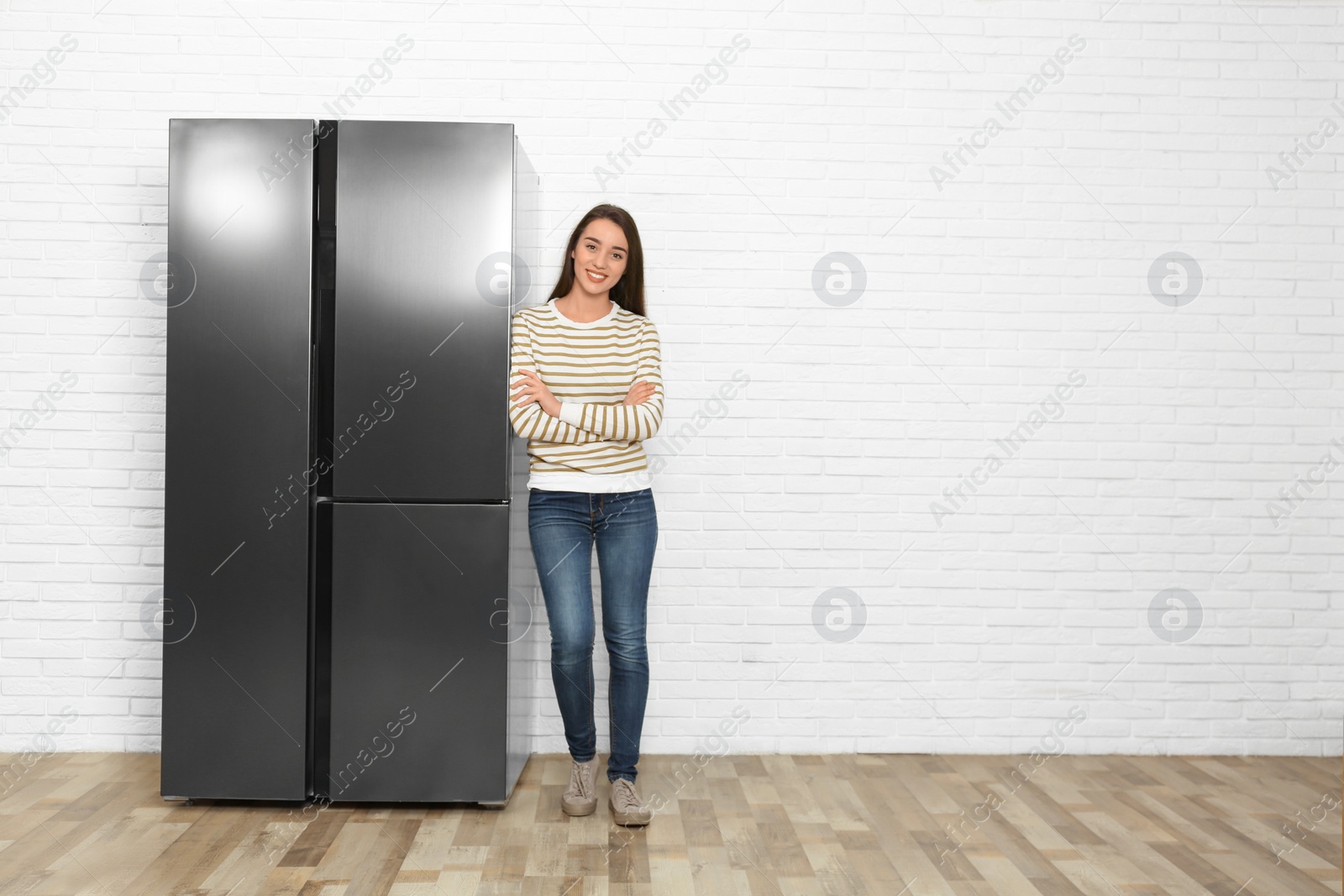 Photo of Happy young woman near refrigerator indoors, space for text