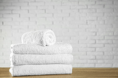 Photo of Clean bath towels on wooden table near white brick wall