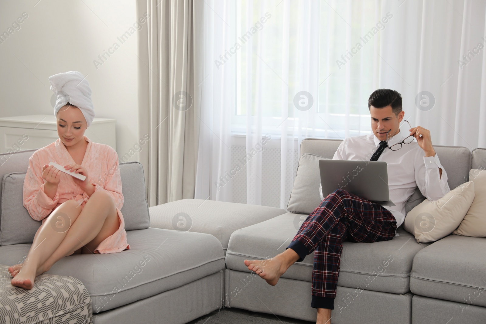 Photo of Man working on laptop while his wife relaxing in living room. Stay at home concept