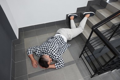 Photo of Unconscious man lying on floor after falling down stairs indoors, above view