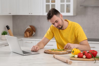 Photo of Man making pizza with cooking online course on laptop in kitchen. Time for hobby