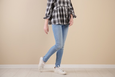 Young woman in stylish jeans near light wall