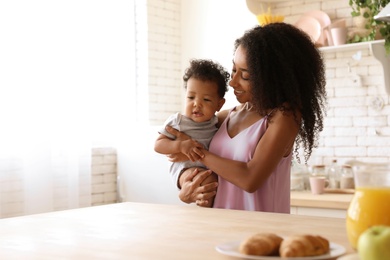 Photo of African-American woman with her baby in kitchen. Happiness of motherhood