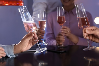 Woman filling glass with champagne and her friends at table in bar, closeup