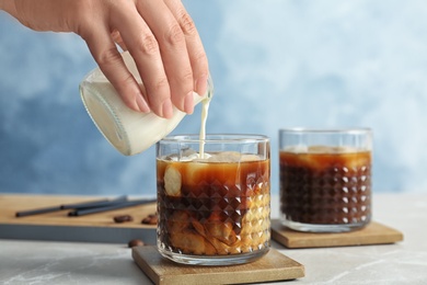 Photo of Woman pouring milk into glass with cold brew coffee on table