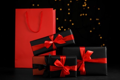 Photo of Gift boxes and paper shopping bag against blurred lights. Black Friday sale