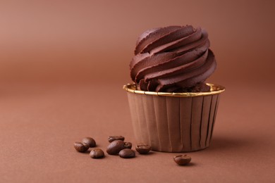 Photo of Delicious chocolate cupcake and coffee beans on brown background, closeup. Space for text