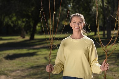 Photo of Happy woman with young trees ready for planting outdoors on sunny day